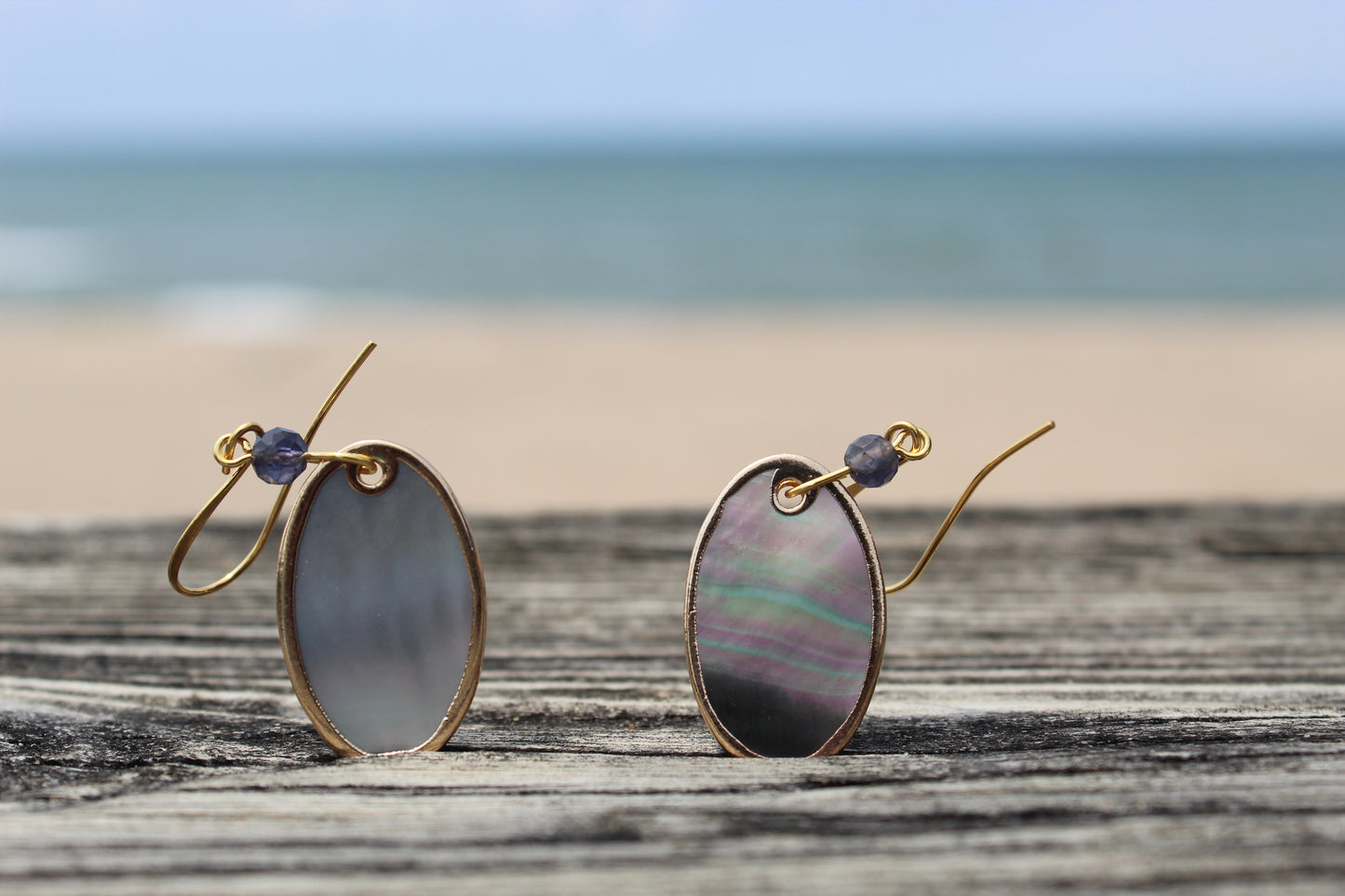 Iolite and gold edged shell drop earrings styled near shoreline