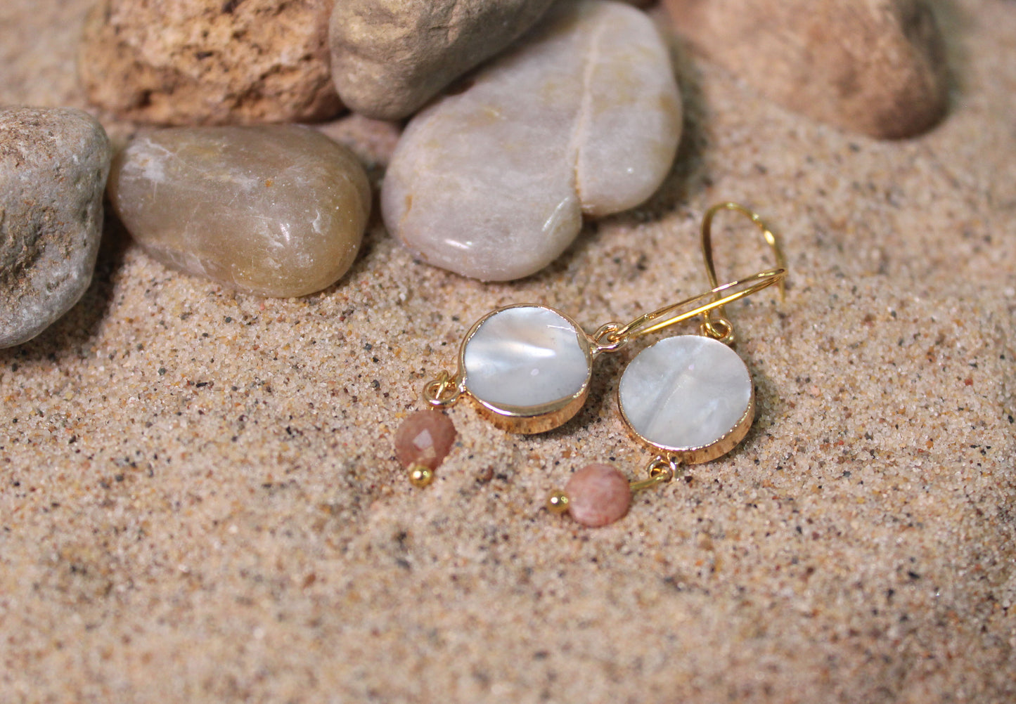 Sunstone and mother of pearl gold drop earrings styled on coastal stones