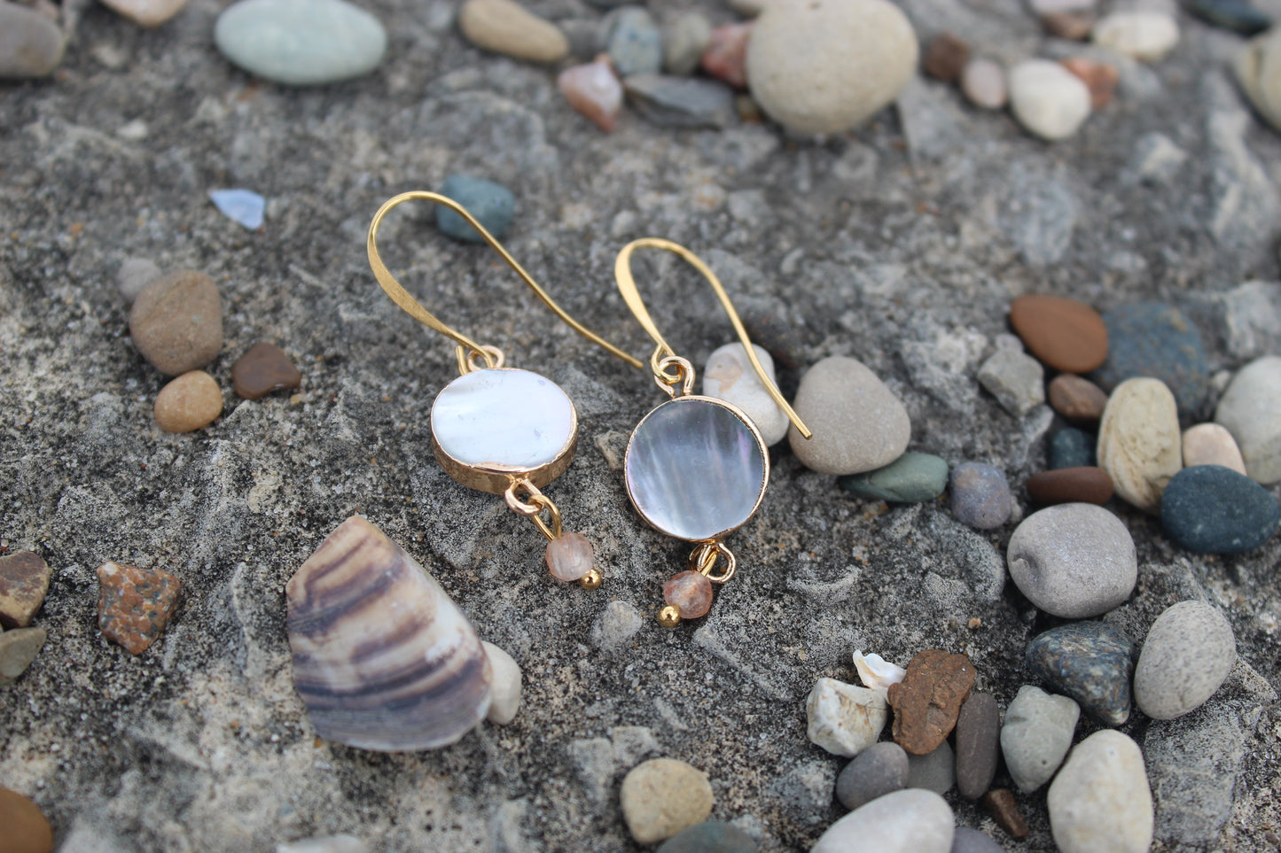 Rare Oregon sunstone and mother of pearl gold drop earrings styled on coastal stones