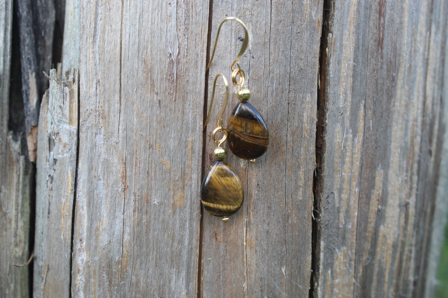 Tiger’s eye gold drop earrings hanging on weathered wood